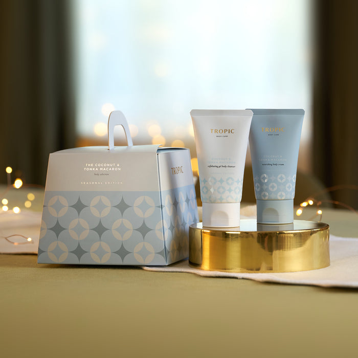 Tropic Coconut & Tonka Macaron exfoliating body cleanser and nourishing body cream on a gold tray beside the patterned seasonal gift bag with fairy lights.