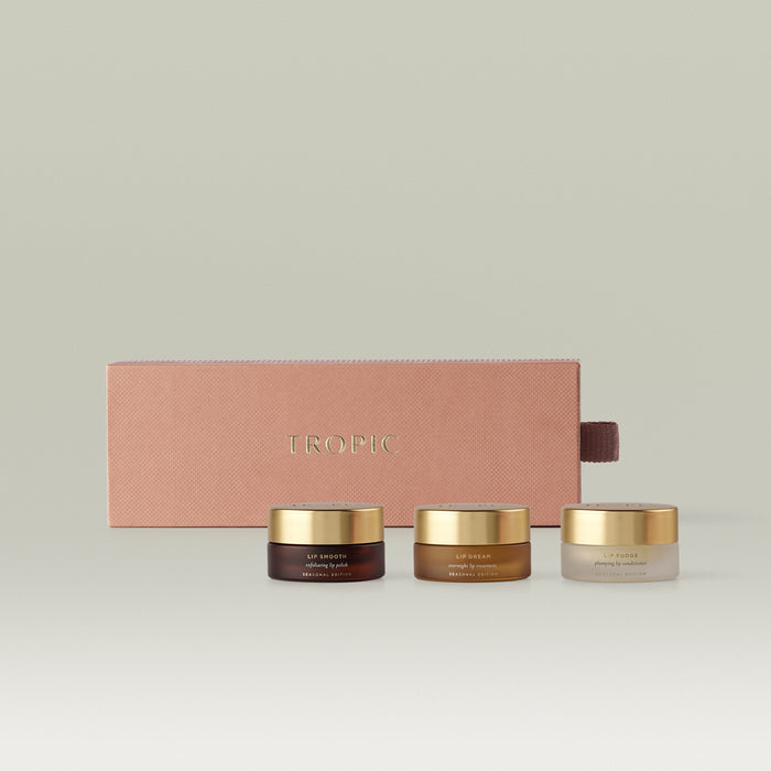 Tropic Seasonal Edition lip care gift set featuring three gold-lidded pots - Lip Smooth exfoliating lip polish, Lip Dream overnight lip treatment, and Lip Fudge plumping lip conditioner - displayed in front of a dusty rose embossed gift box.