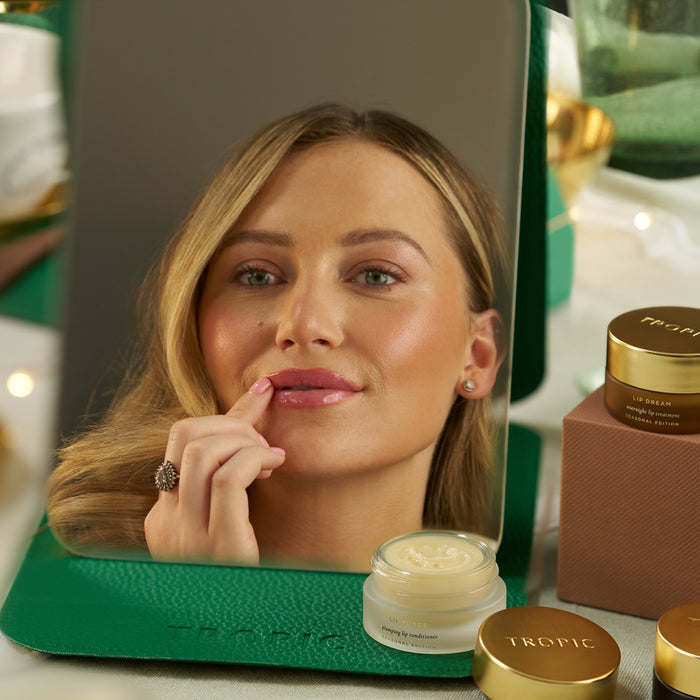 Woman applying Tropic Lip Fudge plumping lip conditioner in a mirror, with Lip Dream overnight treatment alongside.