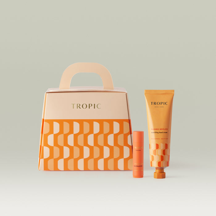 Tropic Body Care Mango Brûlée Seasonal Edition gift set in vibrant orange, including a nourishing lip balm and hand cream, presented alongside a matching geometric-patterned handle gift box.