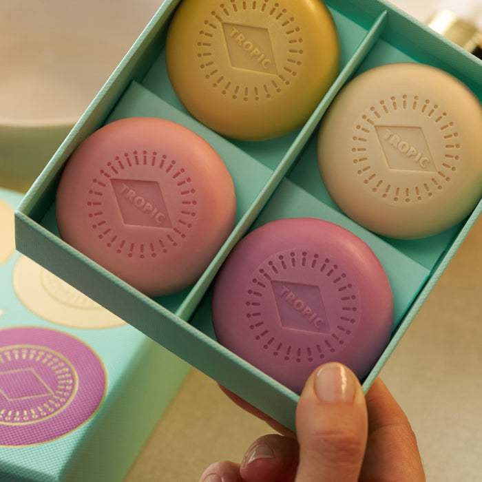 Four Tropic soap bars in yellow, cream, pink and lilac, nestled in a gift box.