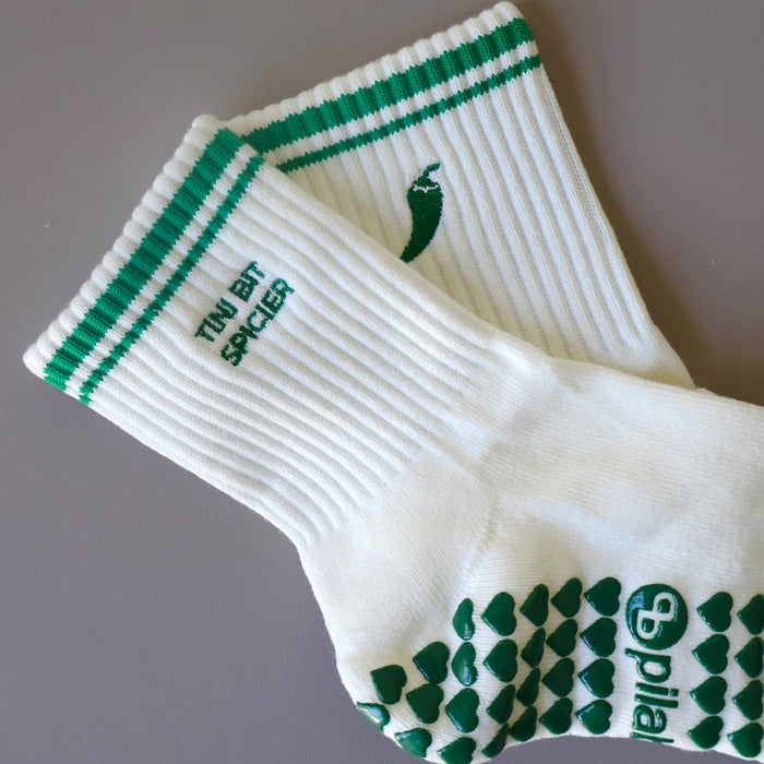 White and green Pilates grip socks with striped ribbed cuffs, embroidered chili pepper detail and green non-slip grips on the soles.